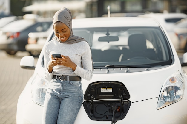 Garota afro-americana carregando carro elétrico no posto de gasolina elétrico