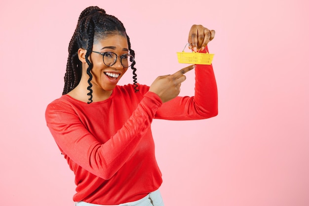 Garota afro-americana com carrinho de compras em fundo rosa O conceito de vendas ou compras lucrativas