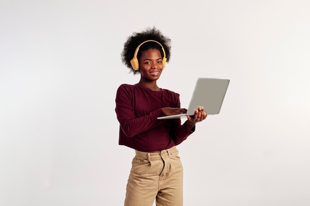 Foto garota afro-americana em poses de suéter marrom com laptop enquanto ouve música.