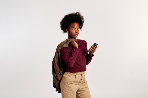 Foto garota afro-americana em poses de suéter marrom com seu telefone inteligente na mão.