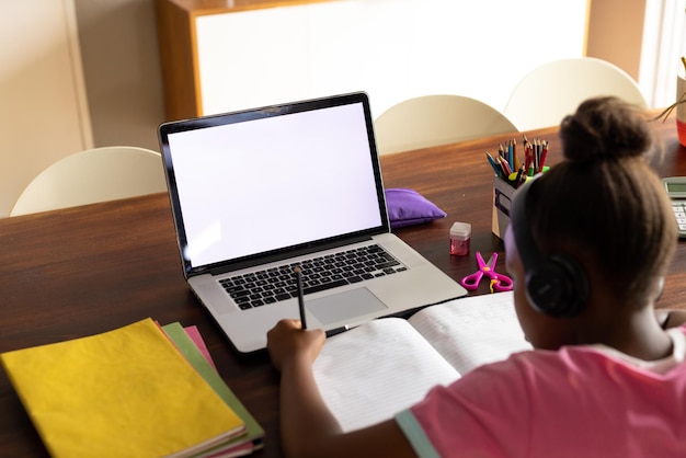 Garota afro-americana fazendo trabalhos escolares usando laptop em casa, copie o espaço na tela