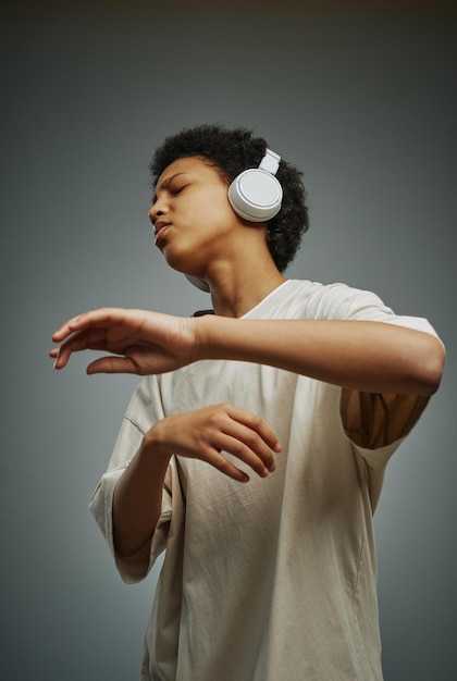 Garota afro-americana jovem em camiseta longa curtindo sua música favorita em fones de ouvido enquanto mantém