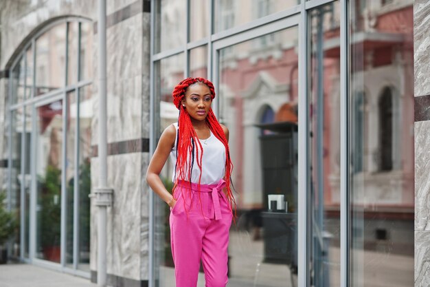 Garota afro-americana na moda em calças cor de rosa e dreads vermelhos posou ao ar livre