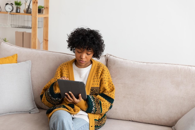 Garota afro-americana segurando a tela de toque do tablet digital digitando página de rolagem em casa mulher com mobi