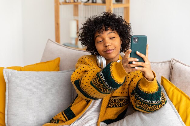 Garota afro-americana segurando smartphone tendo bate-papo por vídeo Blogueira feminina conversando com melhores amigos na rede social Jovem mulher tendo reunião virtual bate-papo online chamada de vídeo em casa