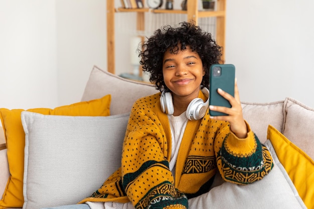 Garota afro-americana segurando smartphone tendo bate-papo por vídeo Blogueira feminina conversando com melhores amigos na rede social Jovem mulher tendo reunião virtual bate-papo online chamada de vídeo em casa