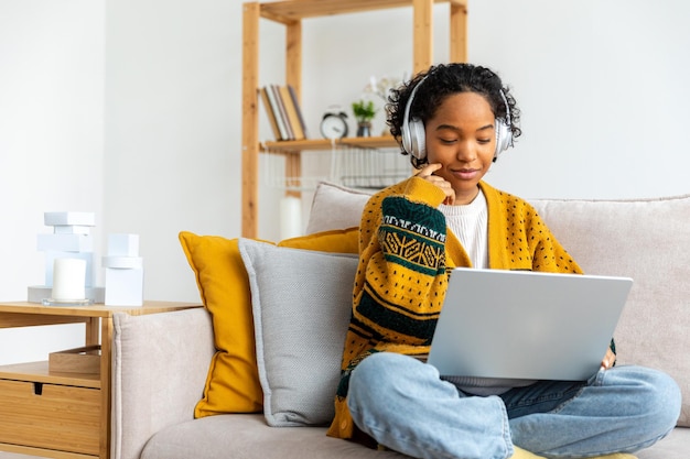 Garota afro-americana usando laptop no escritório em casa olhando para tela digitando conversando lendo escrevendo