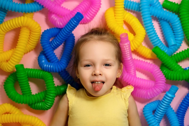 Garota alegre e feliz mostra a língua deitada entre uma pilha de brinquedos coloridos de tubos de pop amarrados com um nó