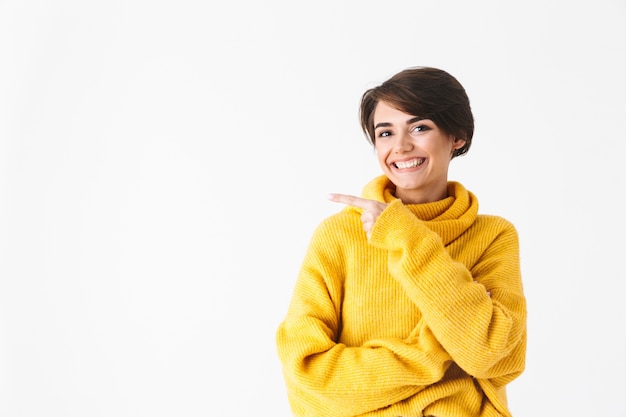 Garota alegre e feliz usando um capuz em pé isolado no branco, apontando o dedo para o espaço da cópia