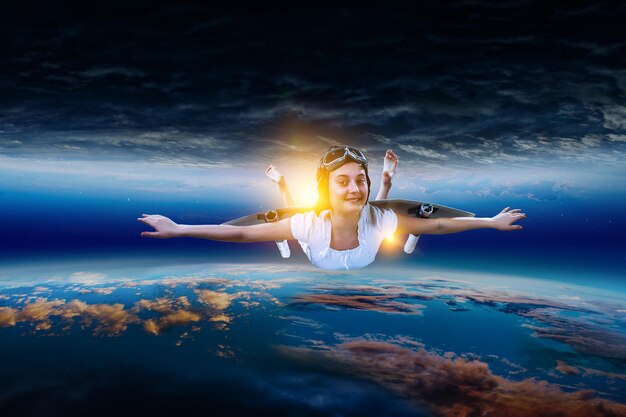 Garota alegre voando com asa de papel auto-feita no espaço. Mídia mista