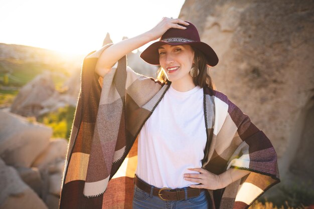 Foto garota alpinista de poncho e chapéu no topo da montanha ao pôr do sol