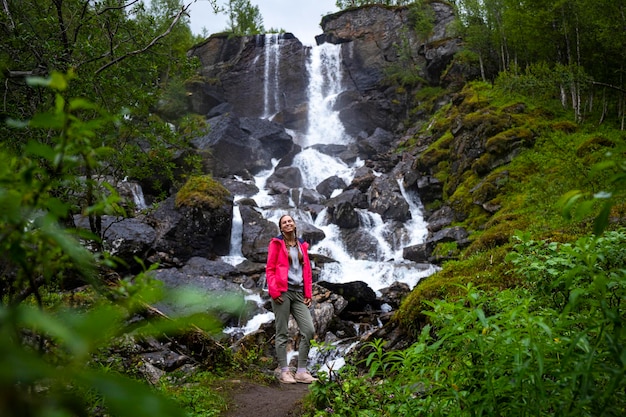 garota alpinista fica sob uma grande cachoeira em cascata no norte da noruega, noruega dura e escura