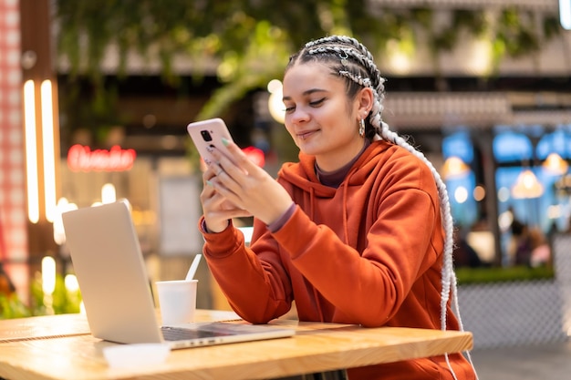 Garota alternativa com tranças brancas usando um computador em um shopping, sorrindo e emitindo uma mensagem de texto