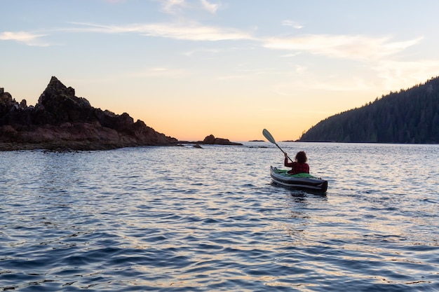 Garota andando de caiaque no Oceano Pacífico durante um pôr do sol nublado de verão