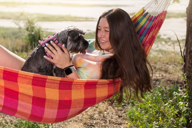 Garota ao ar livre, deita-se em uma rede e segura um cachorro schnauzer em miniatura nos braços, emoções, conceito