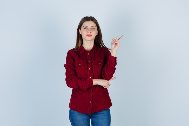 Garota apontando para o canto superior direito em camisa cor de vinho e parecendo orgulhosa.