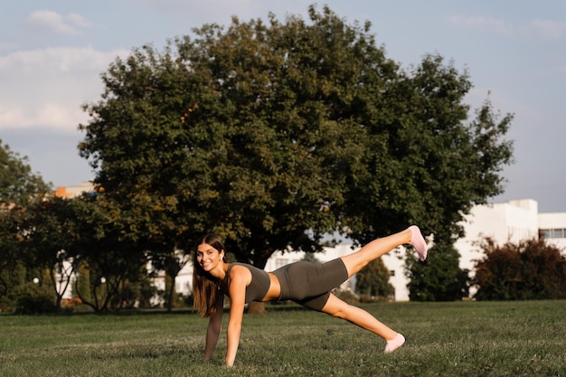 Garota apta treinando na grama verde no parque Treino ao ar livre Estilo de vida esportivo de uma jovem ativa