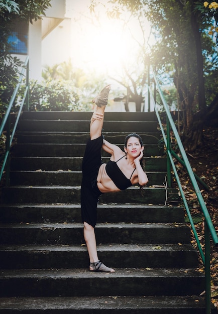 Garota artista de dança fazendo acrobacias e flexibilidades em saltos Garota dançando fazendo flexibilidade nas escadas ao ar livre Retrato de dançarina de salto alto fazendo flexibilidades de ioga