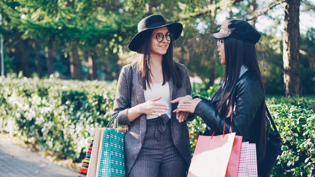 Foto garota asiática atraente está conversando com sua amiga linda morena parada na rua segurando sacolas de compras e rindo cidade de pessoas e conceito de viciado em compras