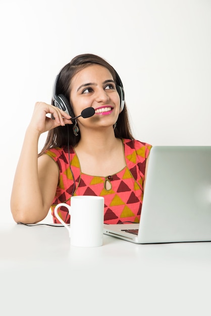 Garota asiática bonita ou funcionário do BPO ou do Call Center falando no fone de ouvido com o laptop na mesa