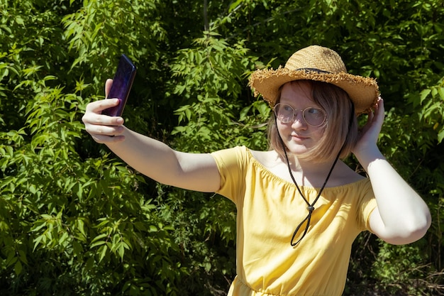 Garota asiática de chapéu de palha de óculos grava vídeos em seu telefone tira selfies se comunica online