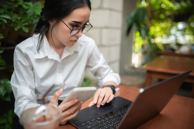Garota asiática legal sentada trabalhando com laptop em uma mesa de madeira na cafeteriaTailândia pessoasHora de relaxar