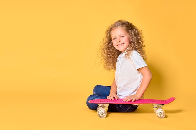 Garota ativa e feliz com cabelo encaracolado, fones de ouvido se divertindo com a prancha, rosto sorridente, carrinho de skate
