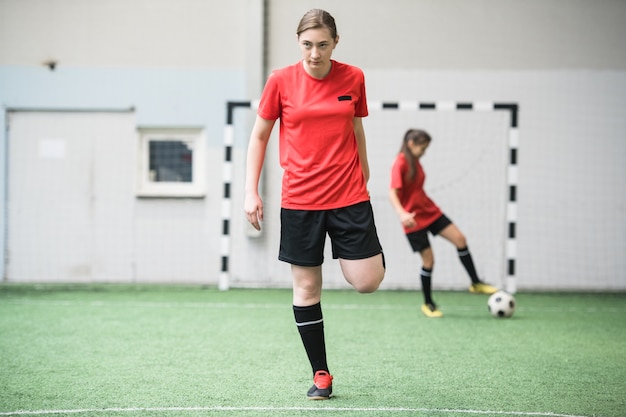 Garota ativa em uniforme esportivo malhando no campo de futebol antes do jogo