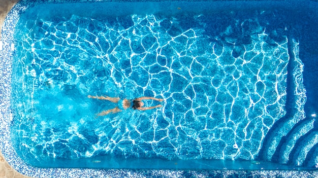 Garota ativa na piscina zangão aéreo vista de cima, jovem mulher nada na água azul, férias tropicais, férias no conceito de resort