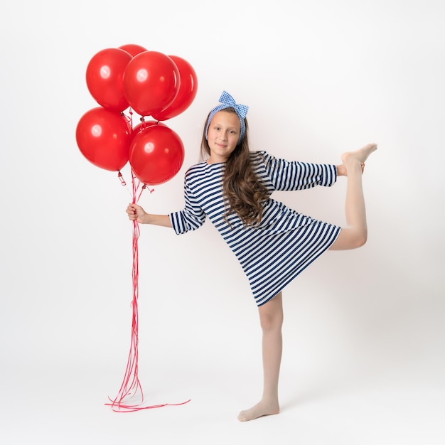 Garota ativa posando segurando um monte de balões vermelhos na mão em pé em uma perna no fundo branco