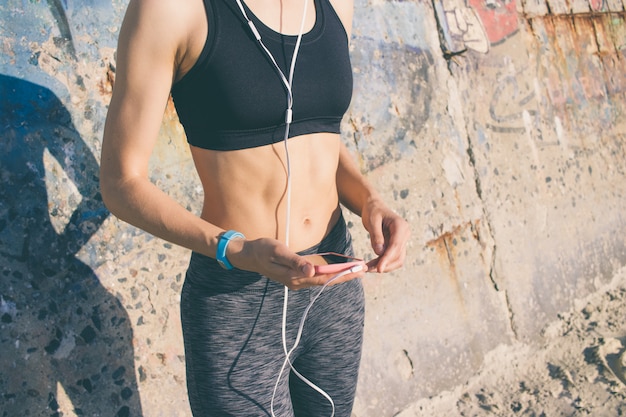 Garota atlética no sportswear é ouvir música com fones de ouvido e segurando um telefone inteligente rosa na mão