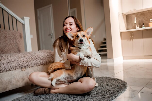 Foto garota atraente abraça e brinca com cachorro corgi em casa welsh corgi pembroke com sua dona no chão da sala de estar