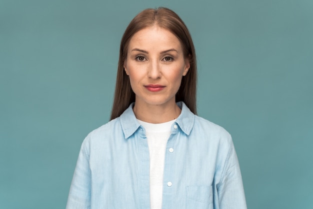 Garota atraente caucasiana, vestindo camiseta branca e camisa jeans, olhando diretamente para a câmera. mulher jovem posando em um fundo de parede azul