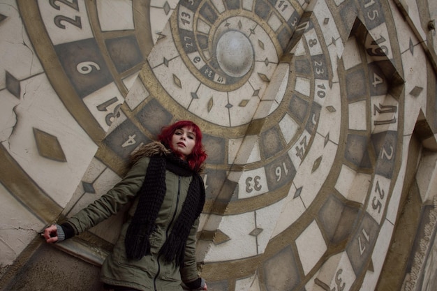 Garota atraente com cabelo vermelho em uma jaqueta de inverno ao lado de uma parede de arte de rua pintada.