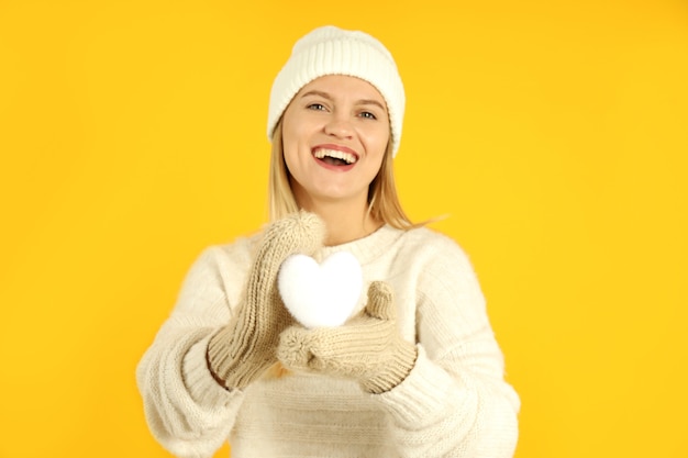 Garota atraente com coração de neve decorativa em fundo amarelo.