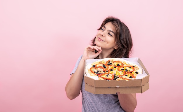 Garota atraente com pizza em uma caixa para entrega em um fundo rosa.