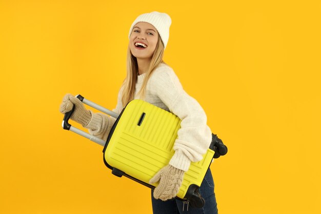 Garota atraente com roupas de inverno com bolsa de bagagem em fundo amarelo.