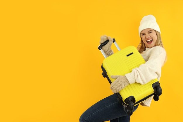 Garota atraente com roupas de inverno com bolsa de bagagem em fundo amarelo.