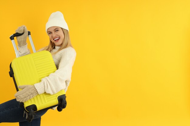 Garota atraente com roupas de inverno com bolsa de bagagem em fundo amarelo.