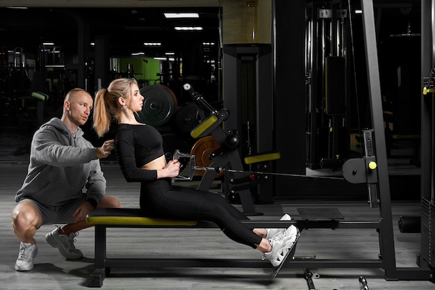 Garota atraente com um personal trainer malhando em uma academia. instrutor de fitness realiza treinamento pessoal.