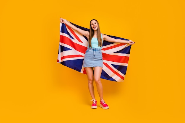 Garota atraente e alegre segurando a grande bandeira britânica isolada sobre um fundo de cor amarela