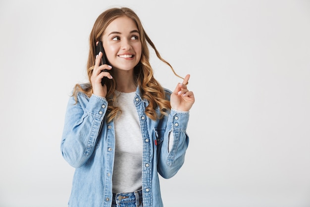 Garota atraente e feliz em pé, isolada sobre o branco, falando no celular