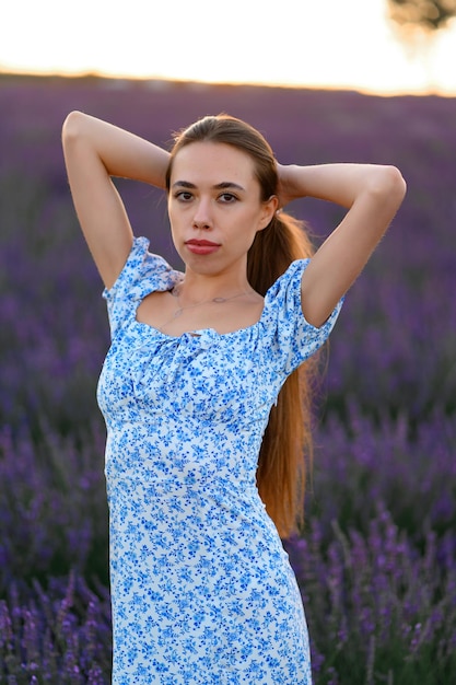 Garota atraente e feliz em um vestido azul em um campo de lavanda ao pôr do sol