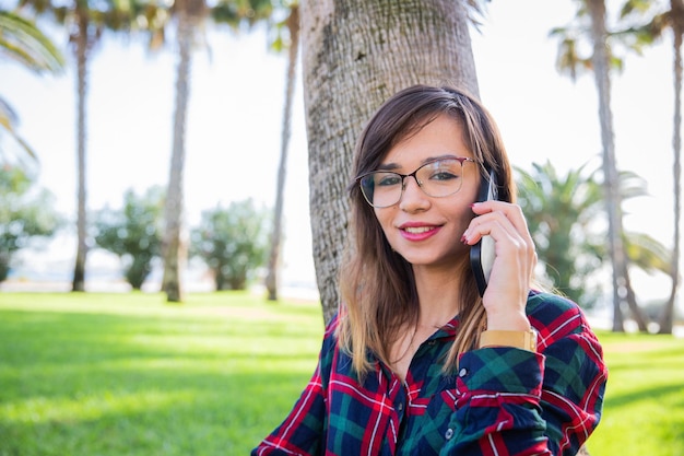 Garota atraente em óculos falando ao telefone em pé em um parque público