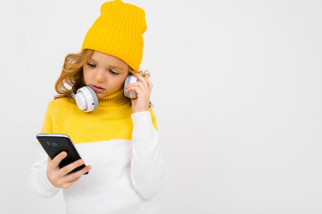 Garota atraente europeia lê mensagens em um smartphone com fones de ouvido no fundo branco pescoço isolado