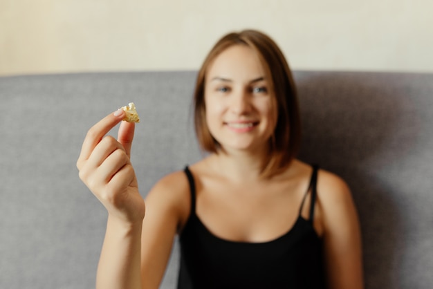 Garota atraente feliz segurando uma pipoca, sentado no sofá cinza.