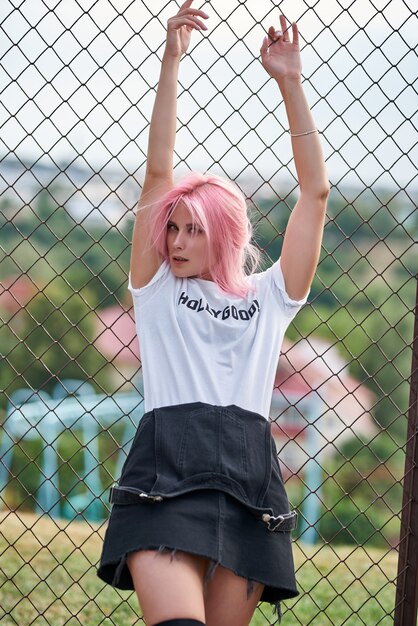 Garota atraente jovem aptidão encostado no muro, ao ar livre. cabelo rosa.