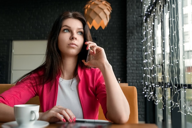 Garota atraente jovem, empresária, falando no celular, sentado sozinho na cafeteria