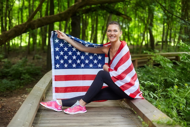 Garota atraente posando com a bandeira americana no parque florestal