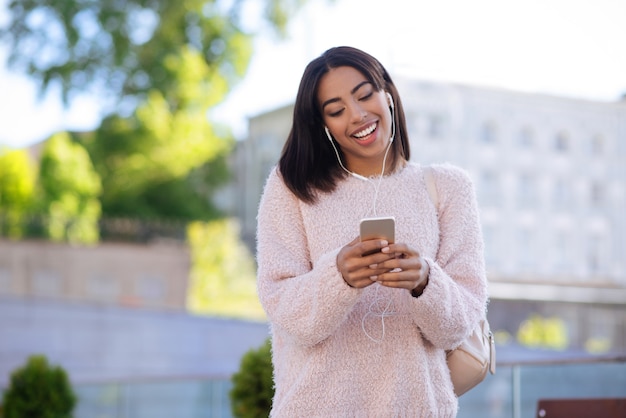 Garota atraente talentosa e fabulosa usando seu smartphone para ouvir meditações enquanto usa fones de ouvido